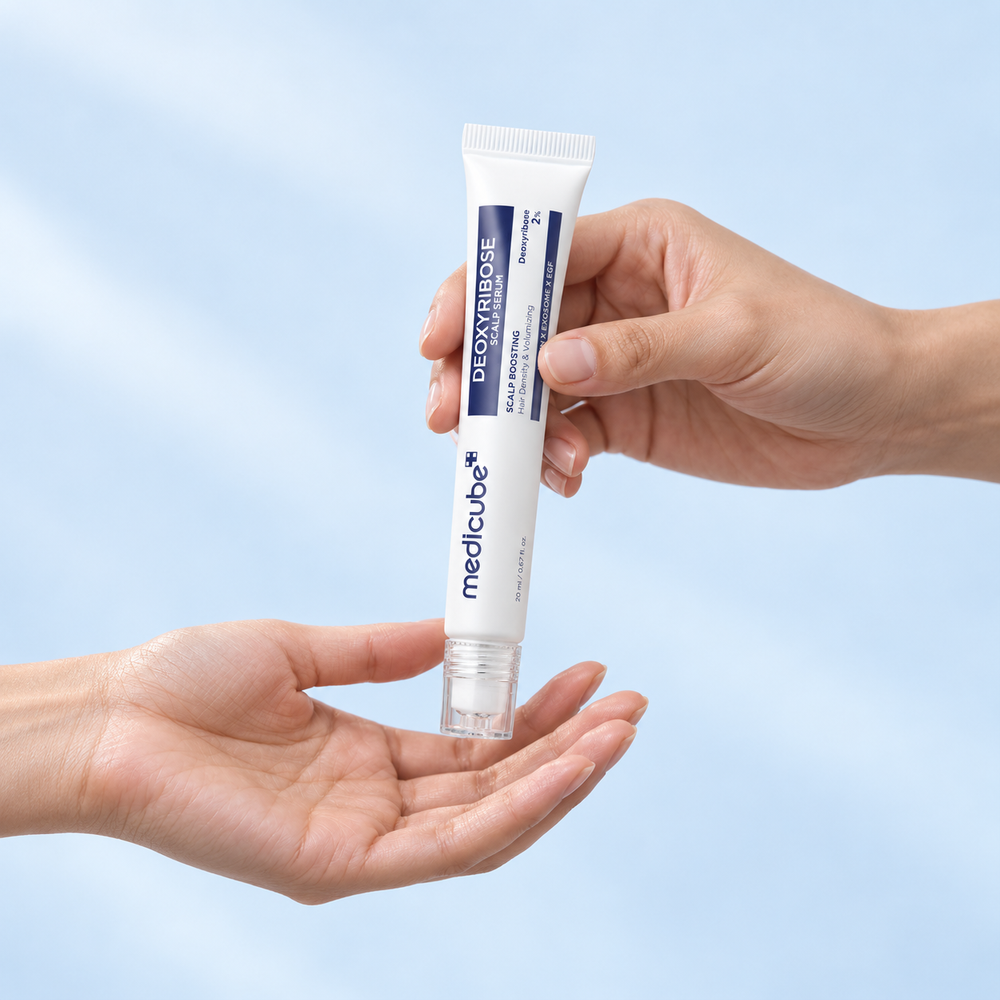 One person handing a Medicube Deoxyribose Scalp Serum tube to another, shown against a pale blue background.